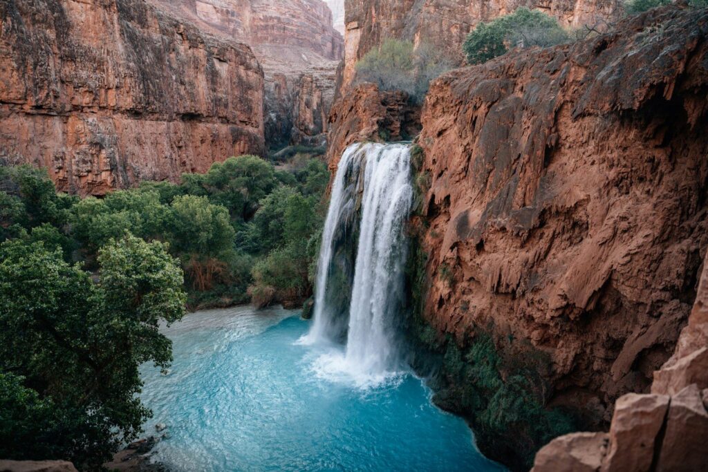 Waterfall cascading into a bright blue pool in a canyon.